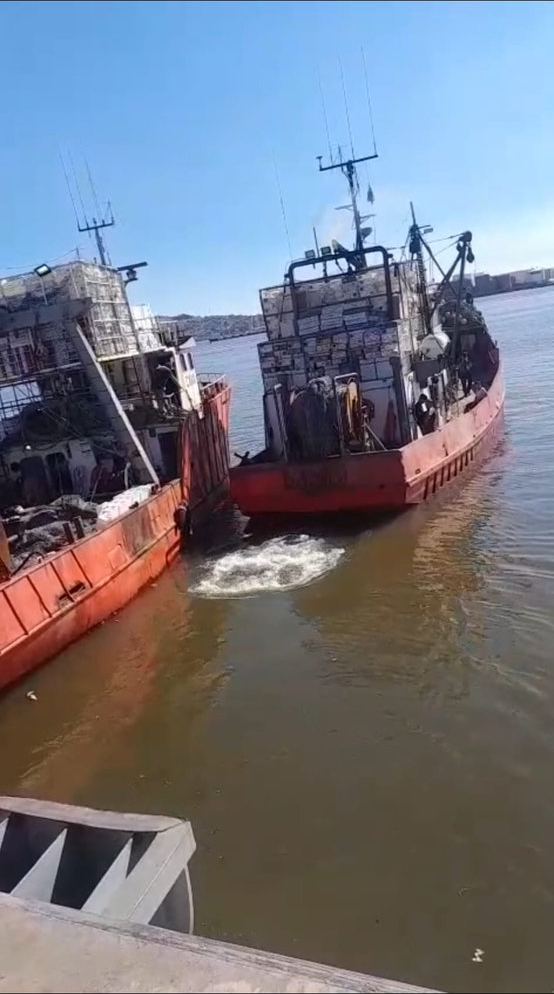 Buque pesquero zarpando junto a otro buque en el puerto